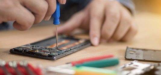Ein Handy wird mit Schraubendreher in seine Einzelteile zerlegt.