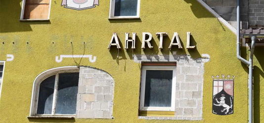 Foto einer Hauswand mit dem Schriftzug "Ahrtal". Fensterlffnungen sind provisorisch zugemauert.